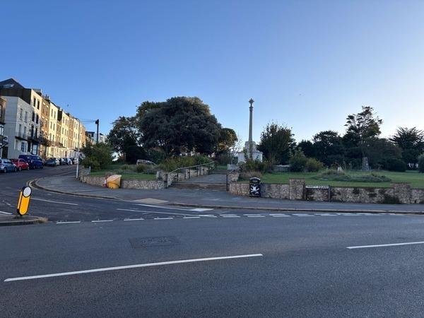 A quiet street corner with a stone war memorial set in a grassy park, bordered by terraced houses.